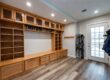Mudroom with extensive wooden storage: upper cabinets, open shelves, shoe cubbies, drawers, and hooks; skis lean by the door nearby.