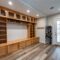 Mudroom with extensive wooden storage: upper cabinets, open shelves, shoe cubbies, drawers, and hooks; skis lean by the door nearby.